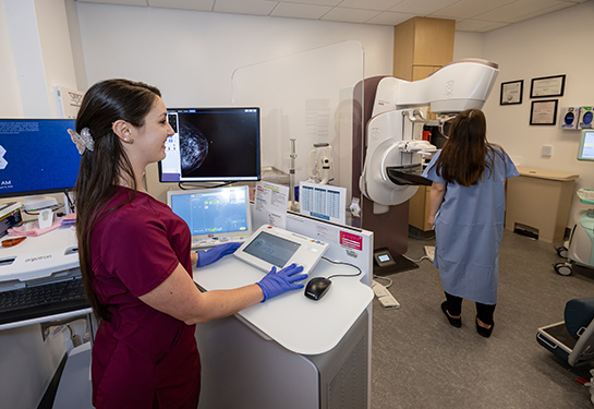 Woman in a red uniform assisting a patient during a mammogram in a medical imaging room.